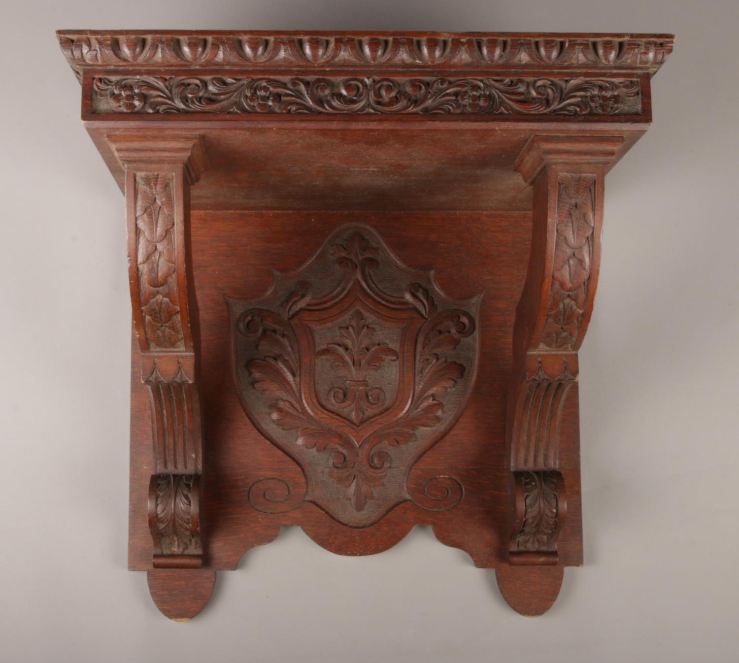 A large carved oak wall shelf, with crest to the underside and floral and foliate border. Height: