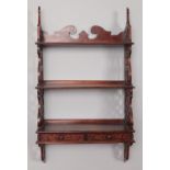 A carved mahogany wall mounted three tiered shelving unit with two bottom drawers.