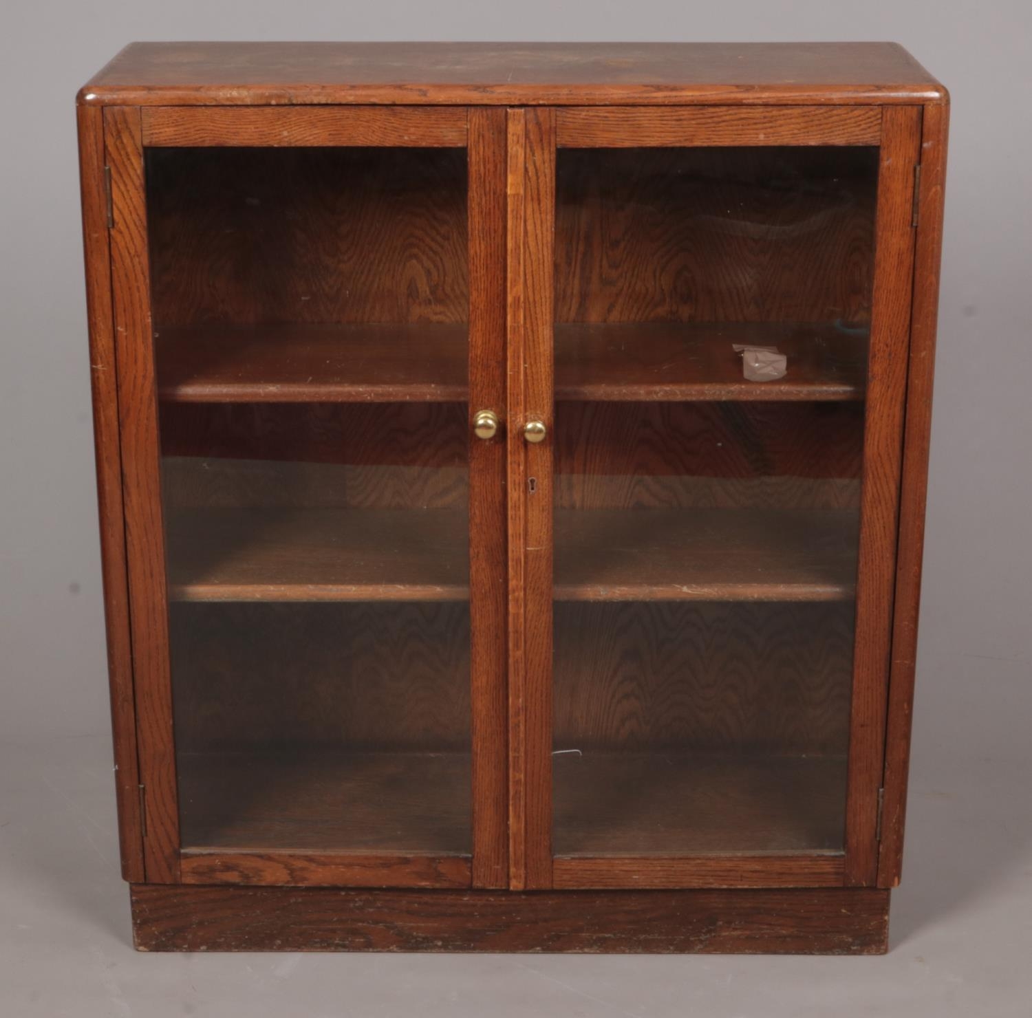 An oak three tier glass bookcase with hinged doors. Height: 104cm, Width: 91cm, Depth: 32cm. Some