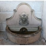 A concrete water fountain/basin with green man mask decoration.