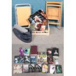 A box of miscellaneous along with a bag of books, a camping table and a folding wooden chair.