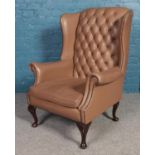 A pale brown button back wing armchair, with brass studs on carved cabriole legs and leather