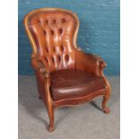A tanned leather deep buttoned armchair with carved scroll arms and legs. Scuffs to the frame.