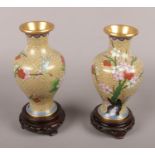 A pair of cloisonné vases on oriental wooden stands.