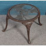 A cast iron glass top garden table with floral decoration.