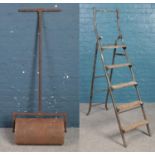 A vintage cast iron garden roller along with a set of vintage shop ladders. Roller 58cm wide.