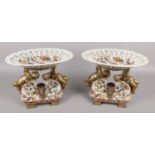 A pair of ceramic and brass centerpieces, with latticework bowls raised by putti figures.