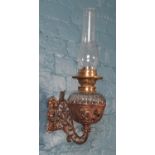 A wall mounting glass font oil lamp. The cast metal bracket having floral decoration.