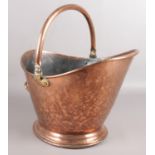A copper coal bucket. Raised on stepped base and has a swing handle.