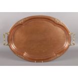 A large oval copper serving tray, decorated with hammered and floral pattern; with brass handles.
