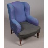 An upholstered wing backed armchair. Comprising of mahogany tapered legs, each with Archibald