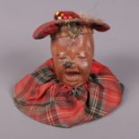 A novelty pin cushion in the form of a child with tartan cap and bib, with a fly on his nose.