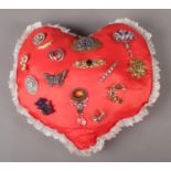 A selection of costume brooches displayed on a heart shaped pillow. Comprising of fifteen in total.