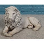 A cast concrete garden statue of a recumbent lion. 62cm long.