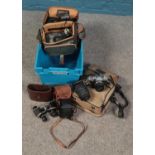 A box of photographic equipment. Includes Olympus OM30, cased French binoculars, Kodak Duaflex,