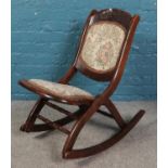 An Edwardian mahogany folding rocking chair with upholstered seat and decorated with carved rose