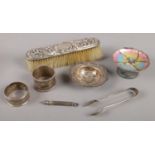 A collection of silver items. Includes enamel dish, pencil, sugar tongs, napkin rings, brush etc.
