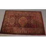 A red ground wool rug with floral borders. 177cm x 119cm.