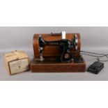 A cased Singer electric sewing machine, with foot pedal and winder.