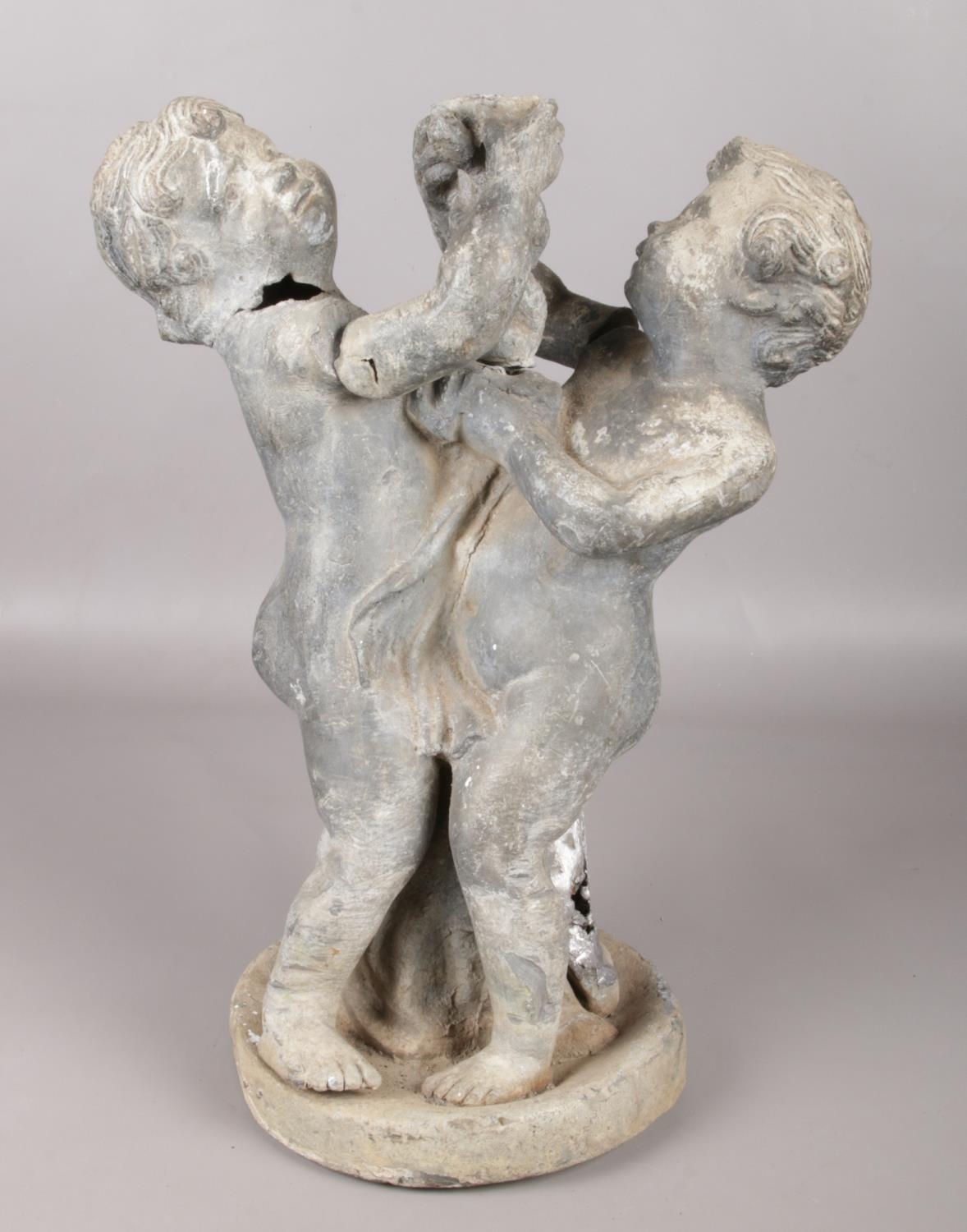 An antique garden statue pair of lead figures on base, clutching a twisted vine. Vine detached,