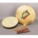 A pair of Bodhran drums, one decorated with a harp, both with protective cases.