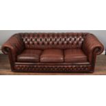 A deep buttoned back and studded arm three seat Chesterfield settee, in brown leather, raised on