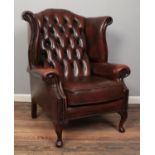 A deep buttoned back and studded winged Chesterfield armchair in brown leather. Minor scuffs to