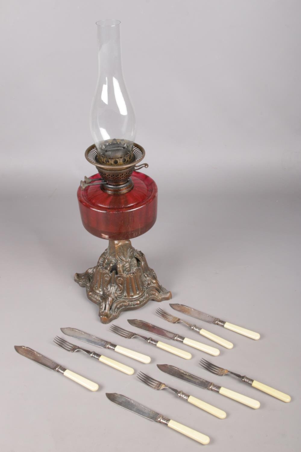 A Victorian cranberry glass oil lamp along with a collection of fish knives and forks.