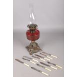 A Victorian cranberry glass oil lamp along with a collection of fish knives and forks.