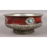 A white metal and hardwood Tibetan bowl, raised on decorative stepped base and turquoise stones to