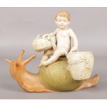 A Royal Dux figure modelled as a baby carrying baskets on the back of a snail. 15cm.