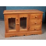 A small pine side cabinet with glass doors and three drawers. (69cm height 108cm width 50cm depth)