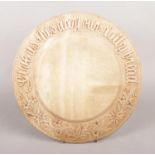 A carved 'Give us this day our daily bread' board. Diameter: 28cm. Slight crack above 'this'.