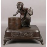 A Japanese bronze desk stand formed as a seated man and a barrel raised on square plinth with