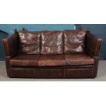 A Parker-Knoll style 3 seat leather sofa, with foldable arms and tassels, raised on casters. Wear to