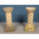 A pair of cast stone bird baths of circular form, with twisted pillars raised on square plinths with