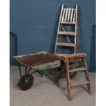 Two sets of wooden ladders along with an iron wheel barrow.