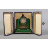 An Art Deco travelling clock in case. Possibly green bakelite housing a gilt metal timepiece.