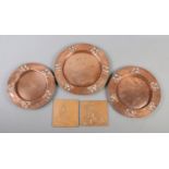Three Arts and Crafts Beldray copper dishes of varying size, together with two copper fronted tiles.