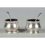 A pair of silver salts, with decorated rims and glass liners; together with silver spoons. Salts