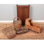 An oak wall cabinet along with a babies rocking crib and wicker baskets.