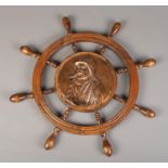 An oak ships wheel with central copper plaque depicting a fisherman smoking a pipe. 60cm diameter.