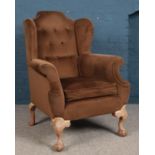 A fabric upholstered buttoned back wingback armchair, with ball and claw front feet.