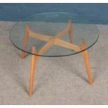 A retro coffee table with wooden legs and circular glass top.