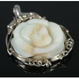 A carved pale green rust and white jade pendant formed as a flower and housed within a scrolling