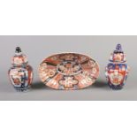A Japanese Imari fluted oval dish along with a pair of similar lidded vases. Chip to dish. Damage