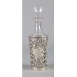 A glass scent bottle with 'JCS' to the body, contained within a silver jacket with pierced floral