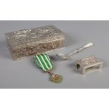 A heavily floral engraved white metal box, containing a mother of pearl handled tea strainer,