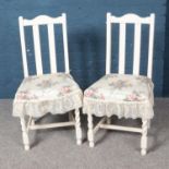 A pair of white painted dining chairs with floral cushions.