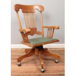 A hardwood swiveling office armchair, with turned supports to back and arms, raised on casters.